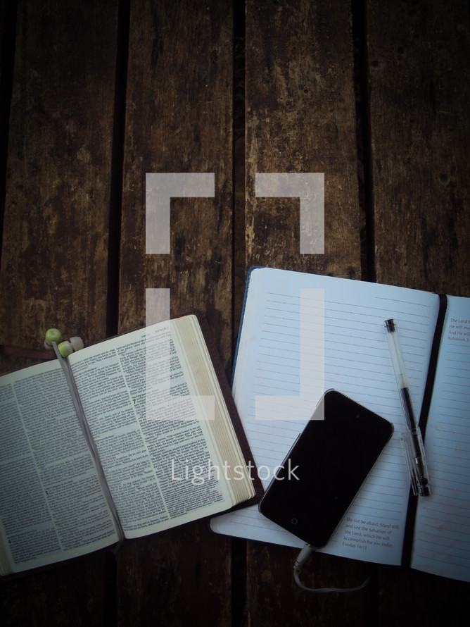 open Bible, notebook, pen, earbuds, and iPhone 