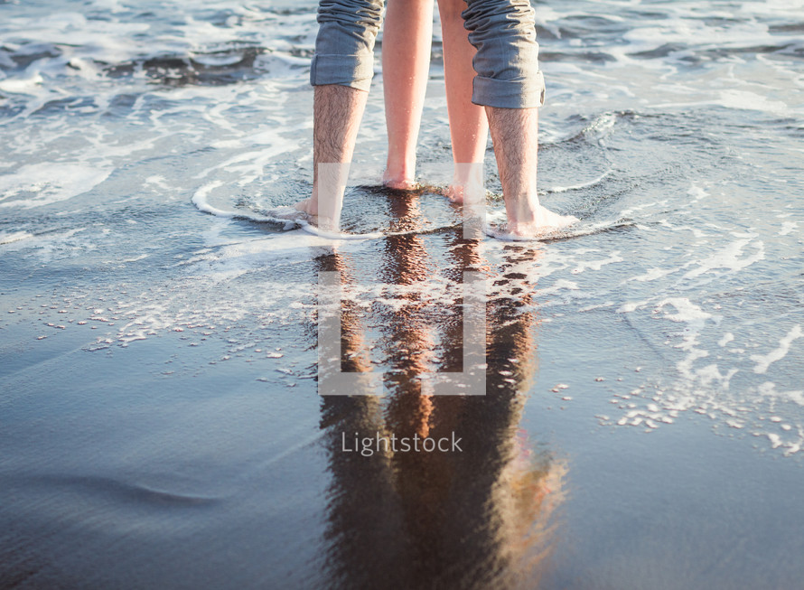 legs of a couple standing on a beach 
