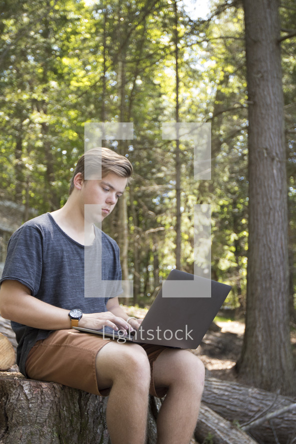 Teenager working on laptop computer in rural wooded environment in woods