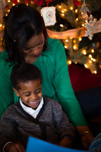 A mother and son reading a book near a Christmas tree 