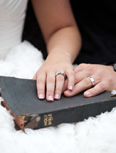 Husband and wife's hands on a tattered Bible.