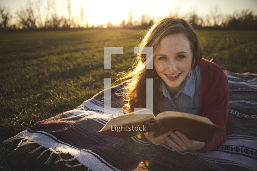 teen girl lying on a blanket in the grass reading a Bible
