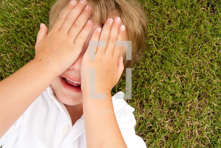 child cover his face lying in the grass 