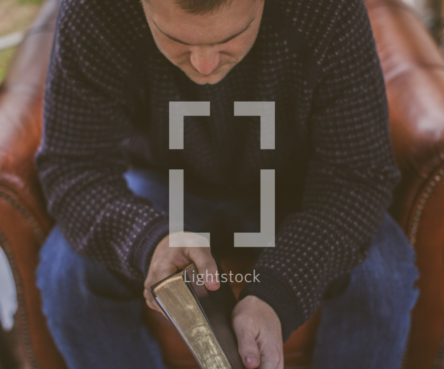 Man sitting a chair praying while holding a Bible.