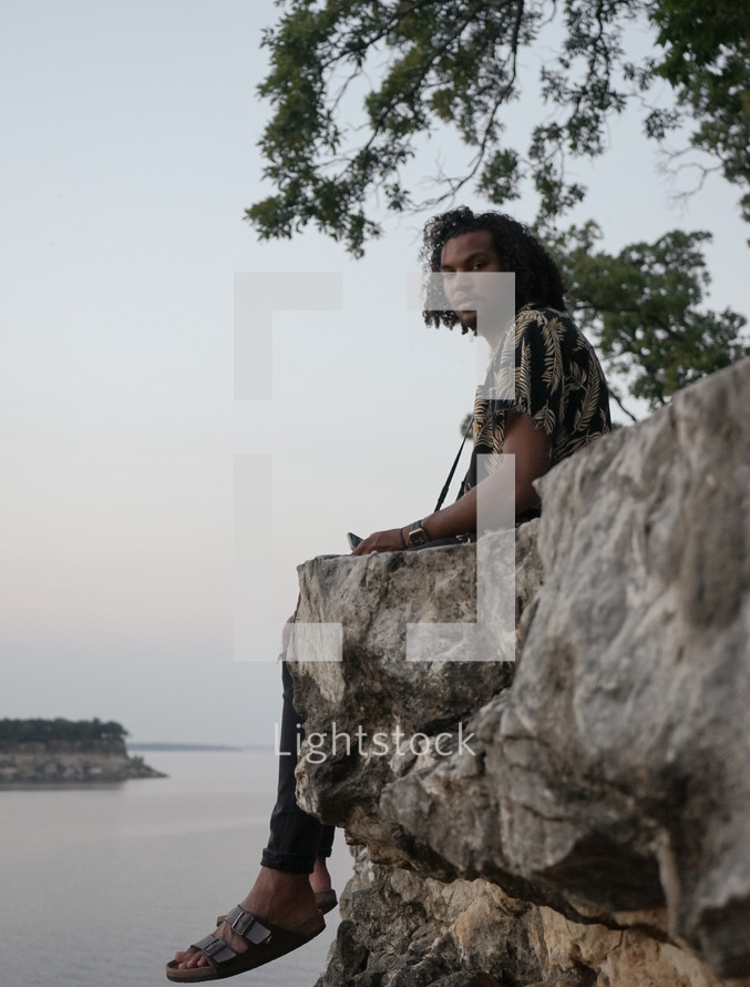 man sitting on the edge of a rock dangling his feet