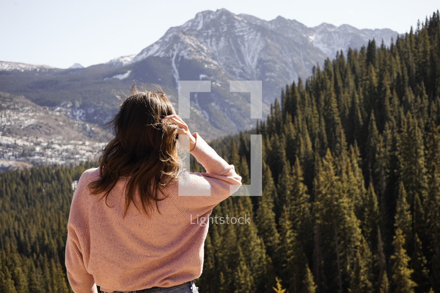 a woman looking out at an evergreen forest 