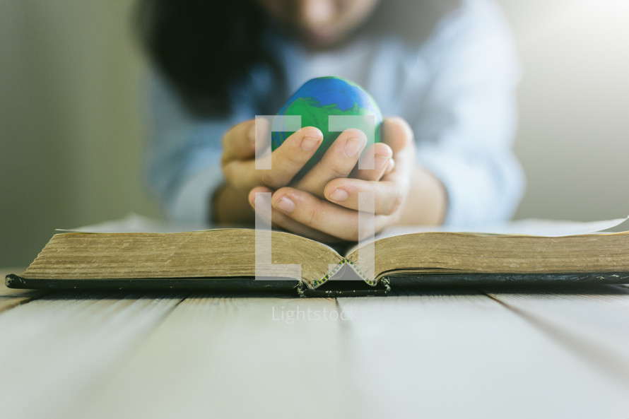a woman holding a globe over the pages of a Bible 
