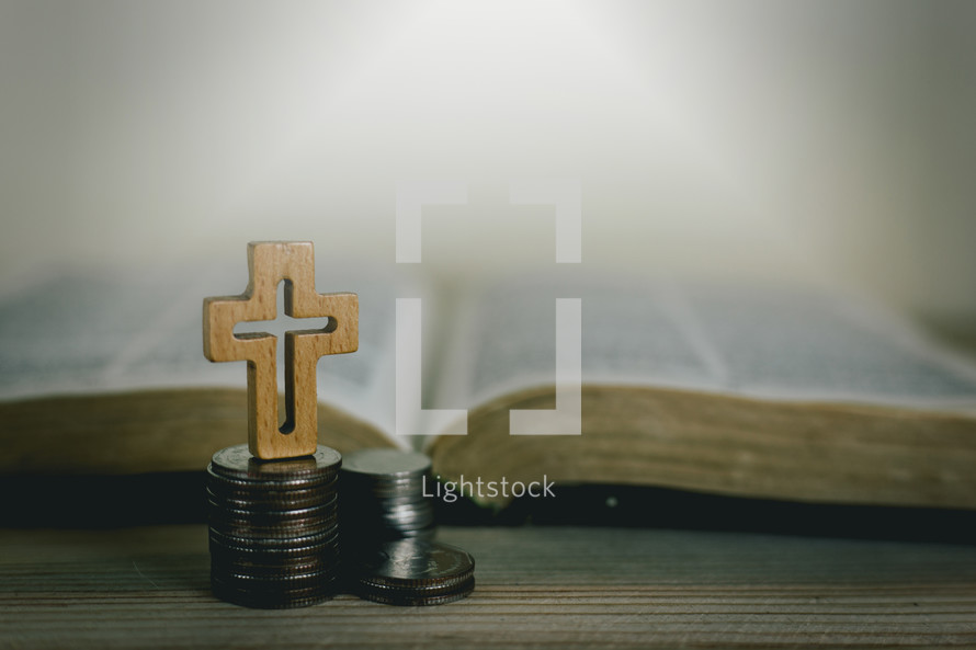 open Bible and cross on a stack of coins 