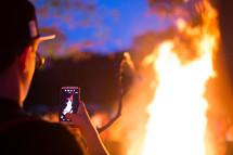 man taking a picture of flames from a bonfire 