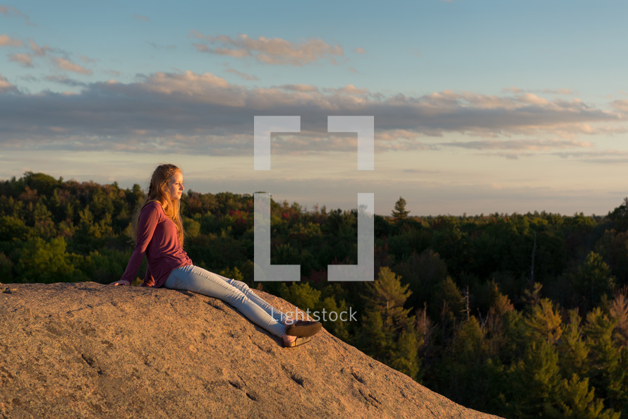 teen girl sitting on a rock on a mountaintop taking in the view 