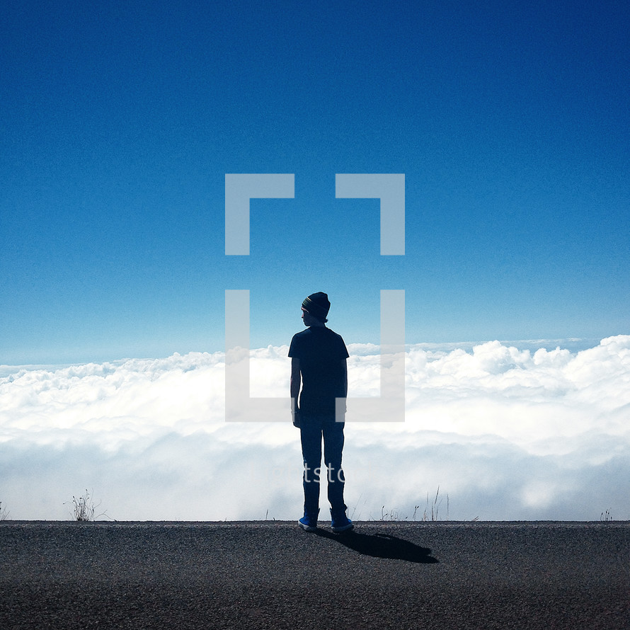 a teenage boy standing on a road above the clouds 