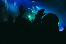 Silhouettes of people in an audience before a stage.