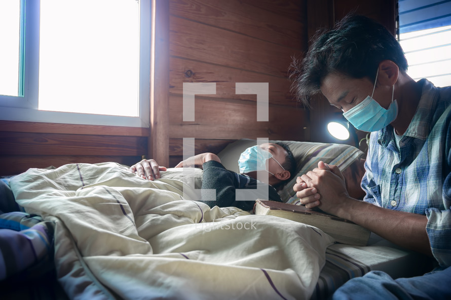 a father praying over a sick boy lying in bed  