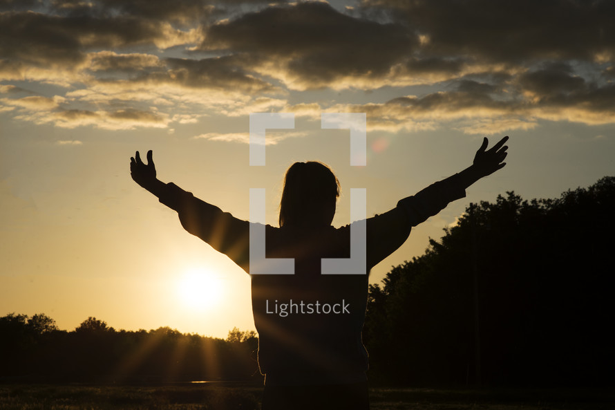 silhouette of a woman with raised hands in praise 