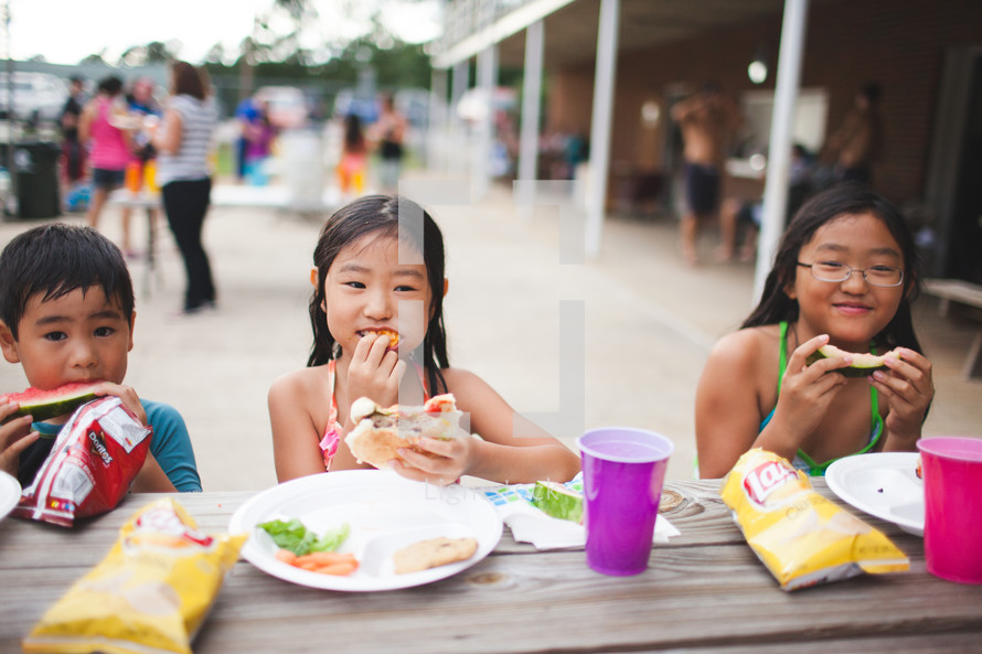 children eating hamburgers at a picnic table 