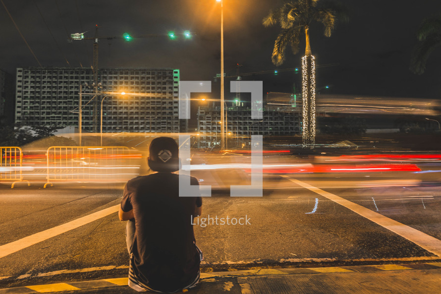 a man sitting on a city curb at night 