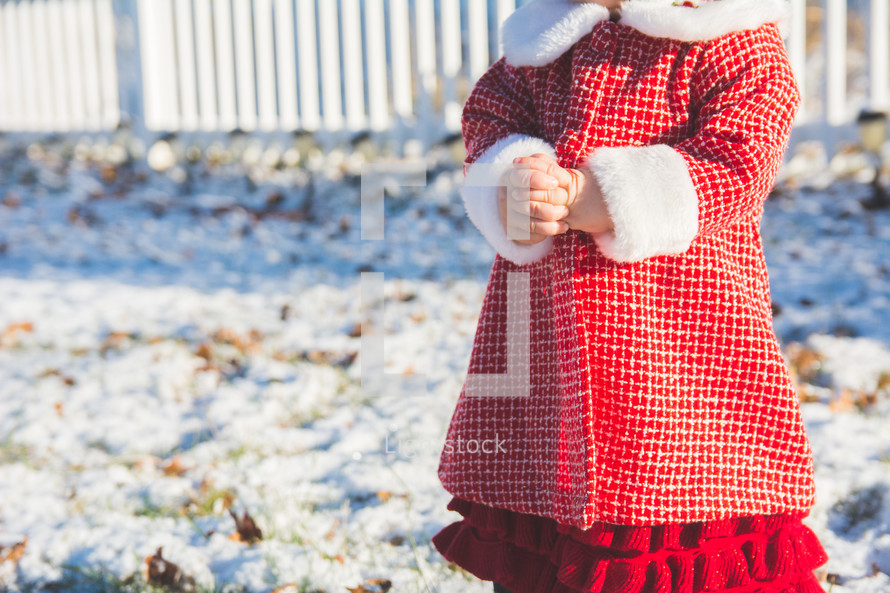 A toddler stands in the snow in winter wearing a red coat