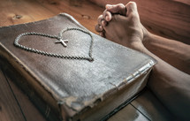 cross necklace in the shape of a heart on a Bible and praying hands 