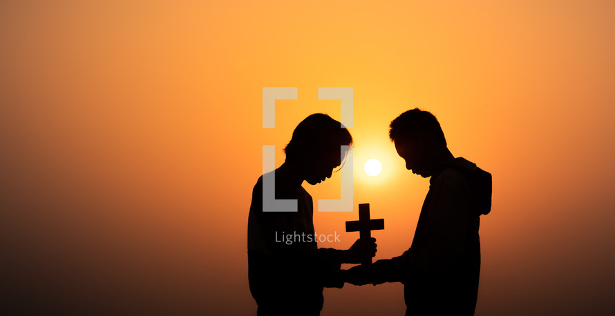 silhouette of two young men holding at cross outdoors at sunset 