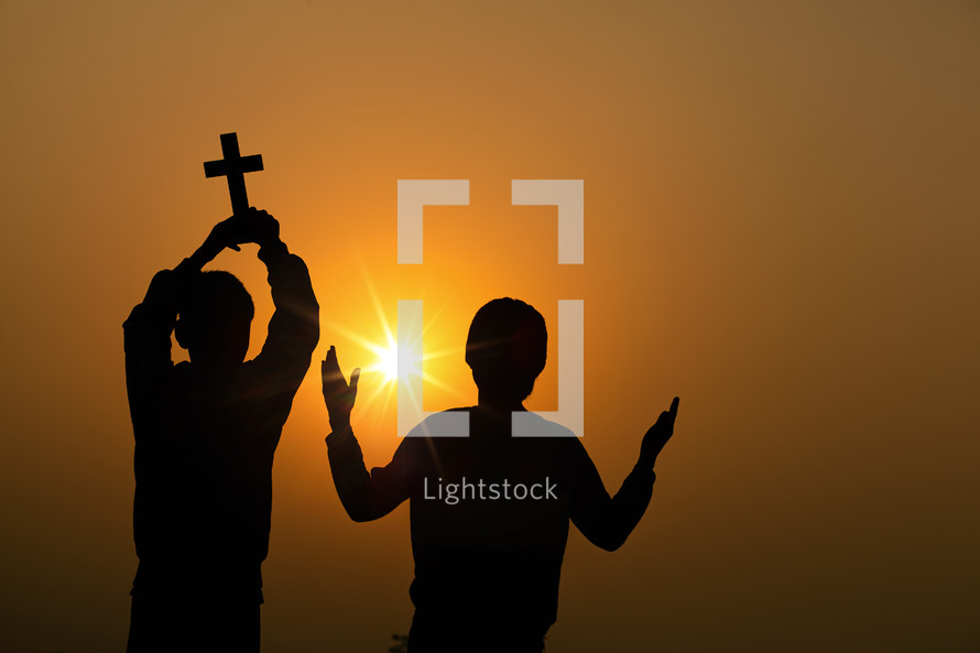 two young boys holding a cross at sunset 