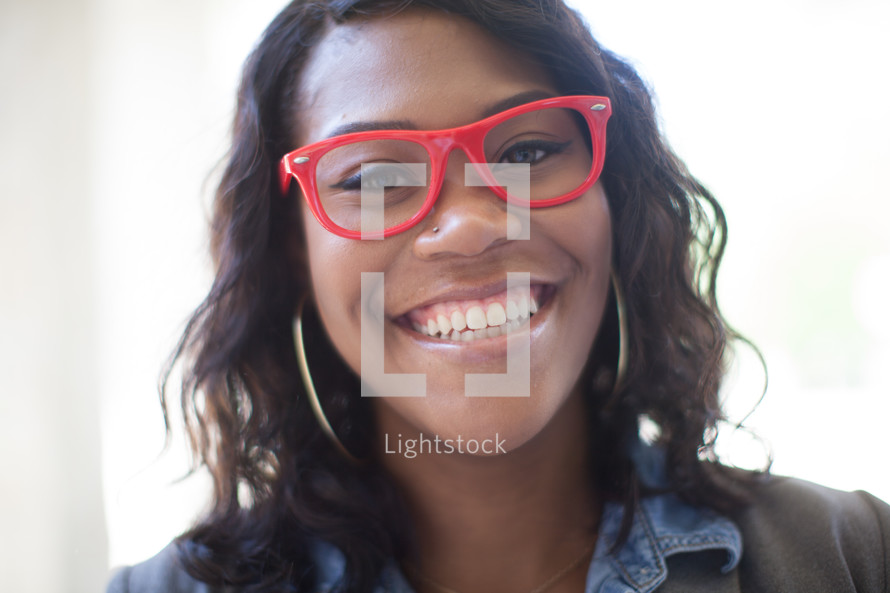 a smiling young woman in red reading glasses 