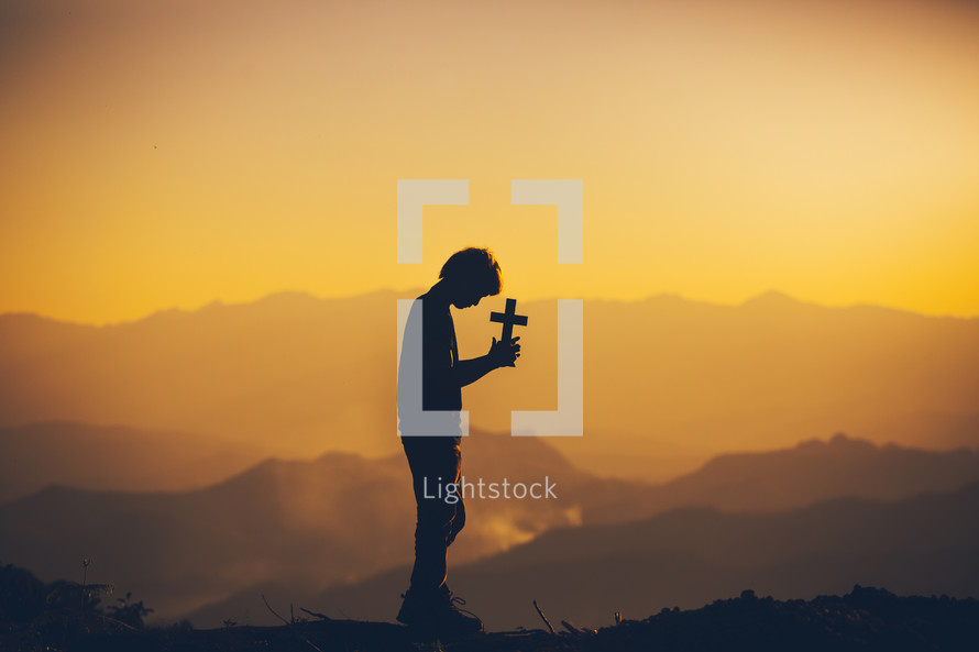 silhouette of a boy holding a cross at sunset 