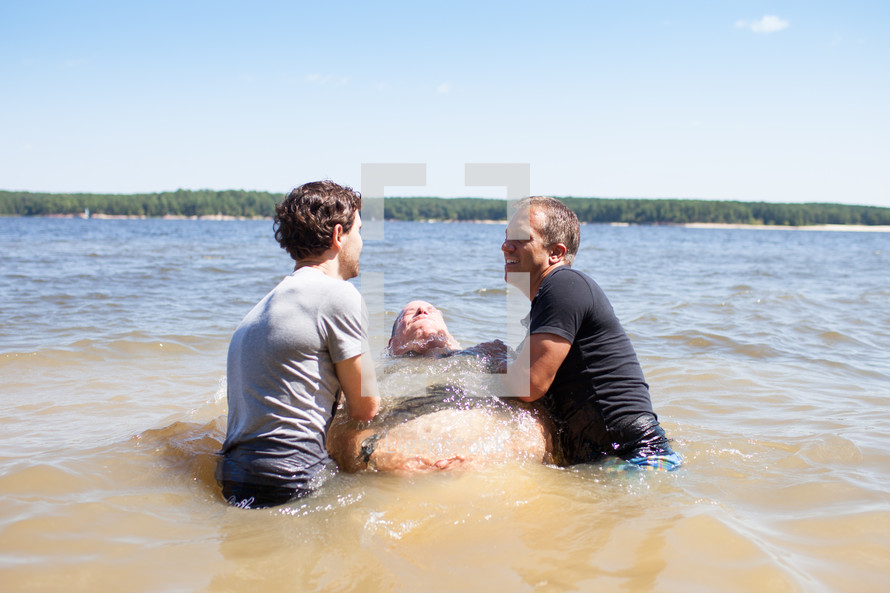 a man being dunked during a baptism in water outdoors 