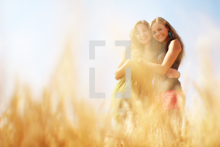 friends hugging in a field of golden wheat 