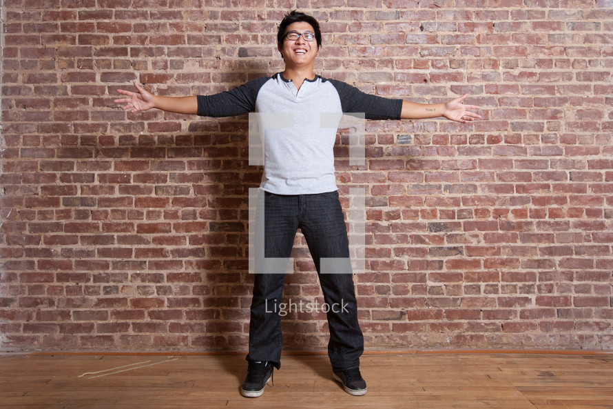 a man standing in front of a brick wall with outstretched arms 