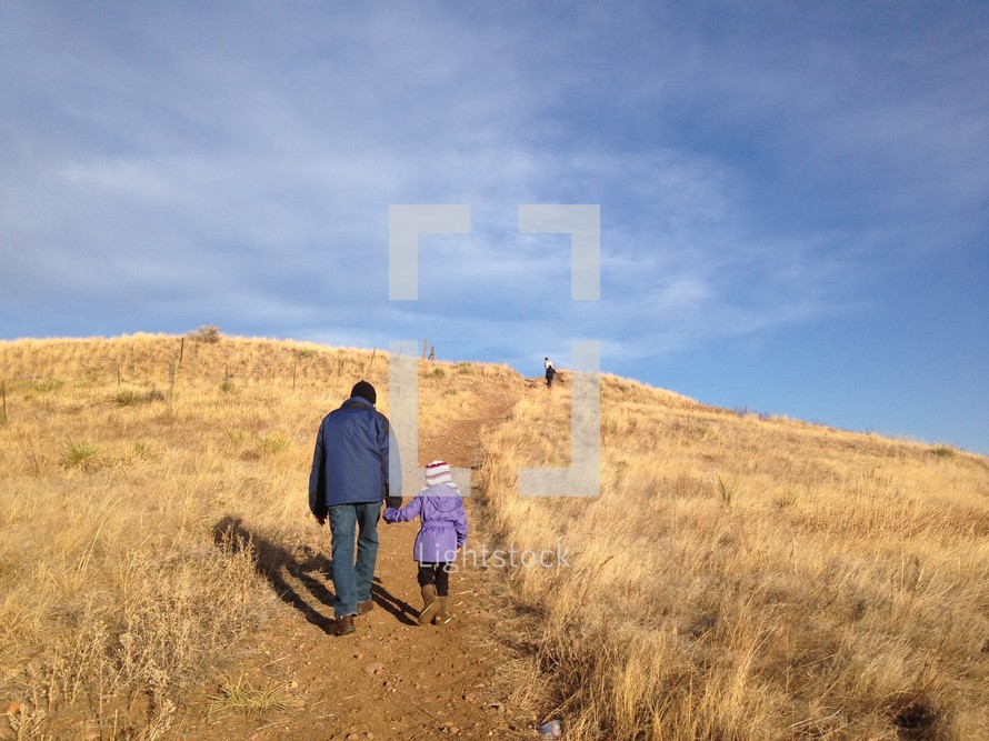 a father and daughter walking up a hill holding hands 