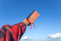 a man holding up a Bible to the sky 