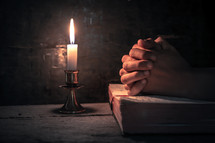 praying hands over and open Bible by candlelight 