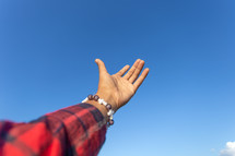 raised hand reaching towards a blue sky 