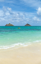 White sand beach on Hawaii coast with kayakers and islands on the horizon