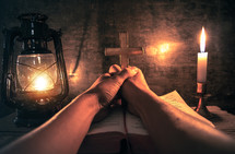 praying hands holding a cross over a Bible 