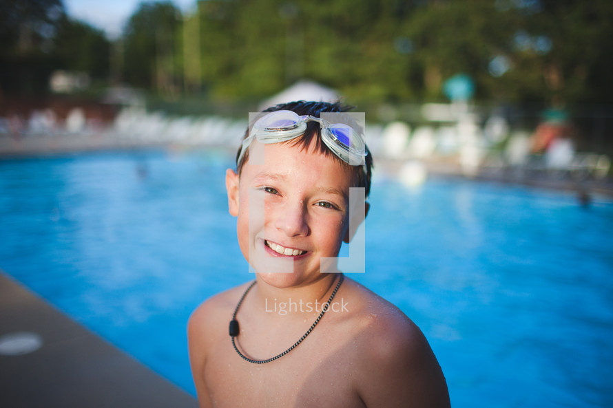 a boy child at a pool with goggles on his head 