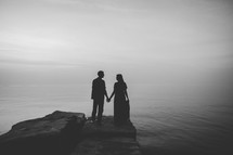 silhouette of a couple holding hands by a shore 