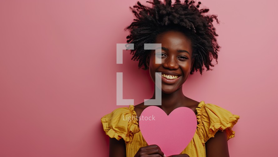 Cheerful african american woman with pink paper heart on pink background