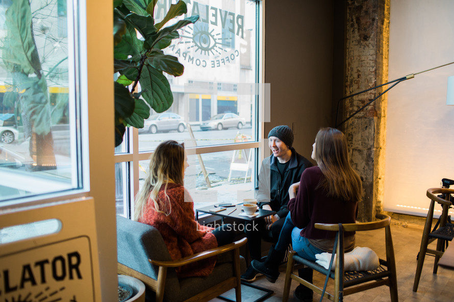 small group of young adults sitting in a window seat talking over coffee 
