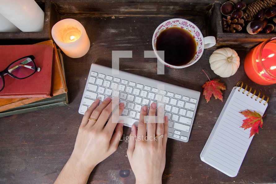 a woman's hands on a computer keyboard on a fall desk 