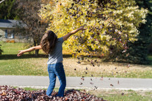 a girl child playing in fall leaves 