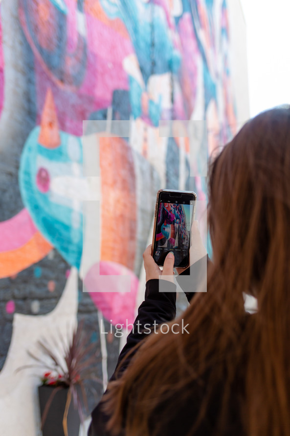 a girl taking a picture of street art with her cellphone 