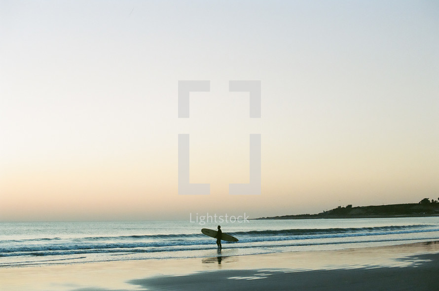 a surfer standing on a beach at sunset 
