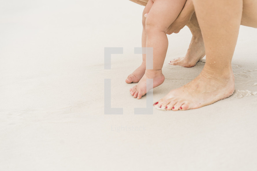 mother and infant with bare feet on a beach 