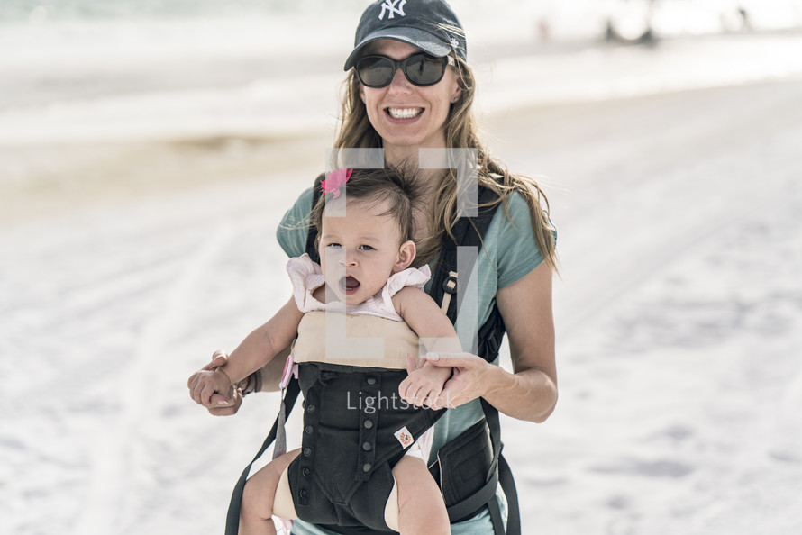 mother walking on a beach with a baby in a baby carrier 
