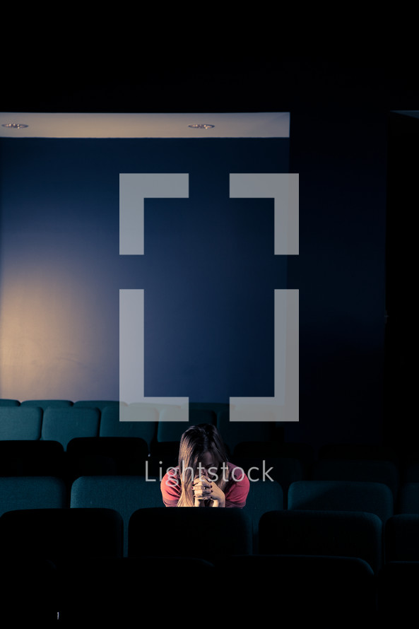 woman sitting in an empty auditorium with her head bowed in prayer