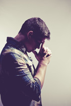 man in prayer with thumbs and index fingers against his forehead