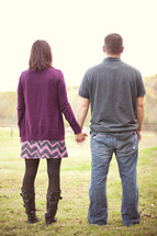 Couple standing in a pasture holding hands.