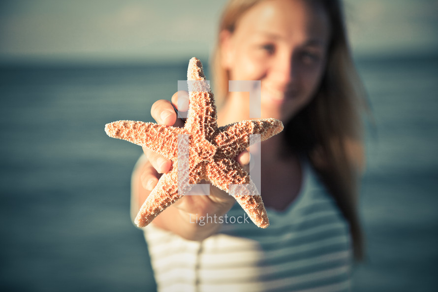 woman holding up a starfish on the beach