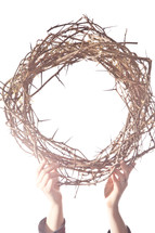 hands lifting up a crown of thorns